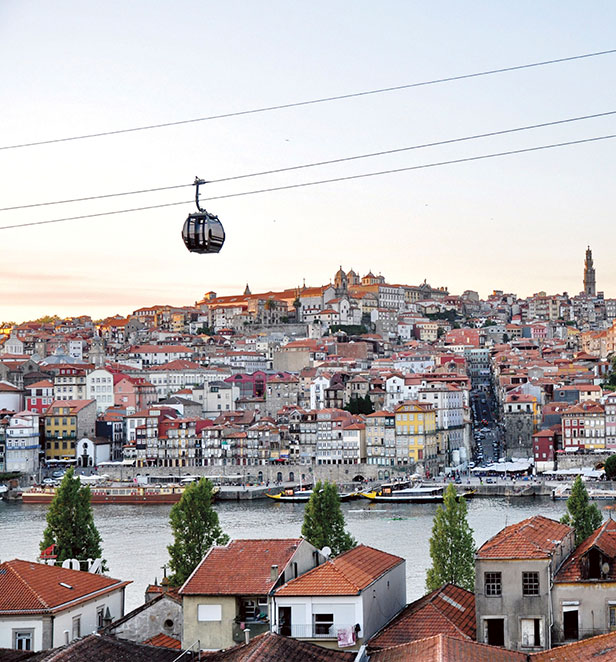 A cable car journey at sunset above the Douro River and many houses and buildings nestled in the town of Porto.   Caption: Cable Car over Porto 